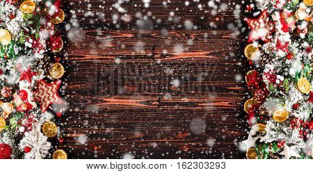Merry Christmas Frame with Snow and wood green pine, colorful baubles, knots with berries,stars, orangesand other seasonal stuff over an old wooden aged background