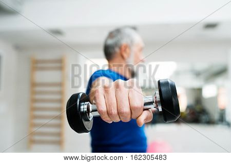 Senior man in sports clothing in gym working out with weights. Close up of hands.