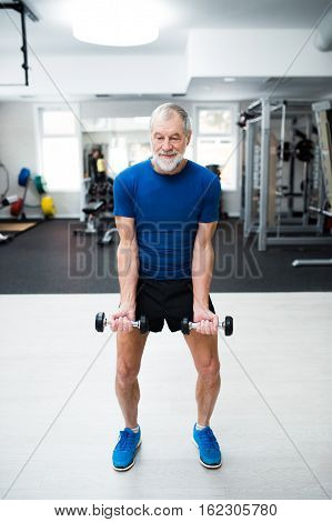 Senior man in sports clothing in gym working out with weights