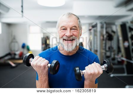 Senior man in sports clothing in gym working out with weights.