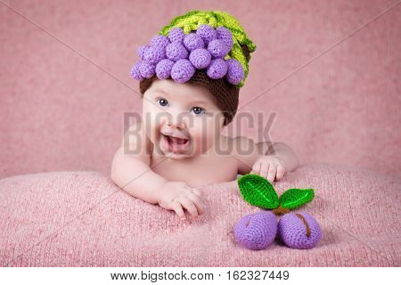 Newborn baby in a knitted cap in the form of grapes.