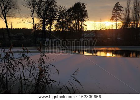 The bright rays of the setting sun glide over the ice of a small lake.