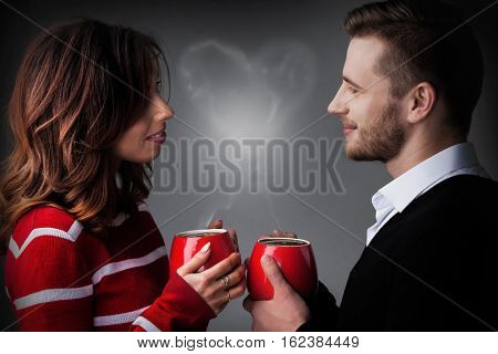 Young couple holding coffee mags with heart shaped steam, Valentine's day concept