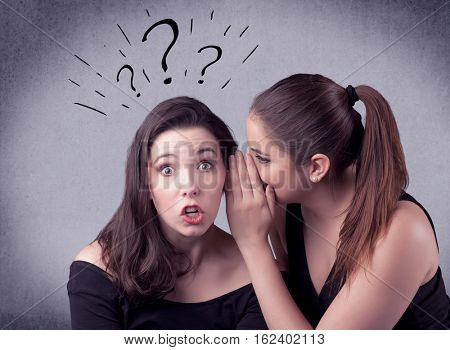 A teenager girl looking confused with drawn question marks above the head, while a girlfriend whispers something in her ear concept.