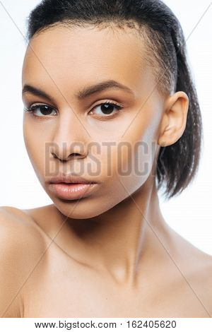 Model in action. Serious unemotional young Negroid woman looking at the audience while standing against white background and posing