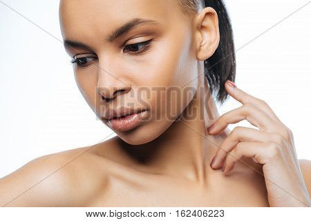 Tender skin. Graceful charismatic young Negroid woman touching her neck while standing against white background and expressing charm