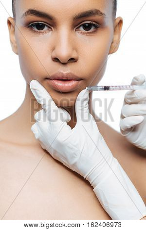 The victim of the beauty. Pathetic involved young Negroid woman standing isolated in white background and expressing confidence while having the injection in her lips