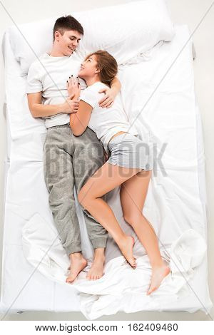 The young lovely couple lying in a white bed, love lconcept, top view