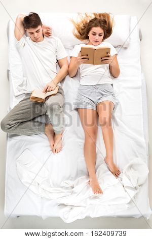 The young lovely couple lying in a white bed with books, love lconcept, top view