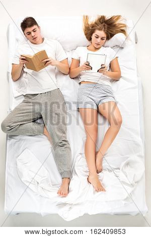 The young lovely couple lying in a white bed with books, love lconcept, top view