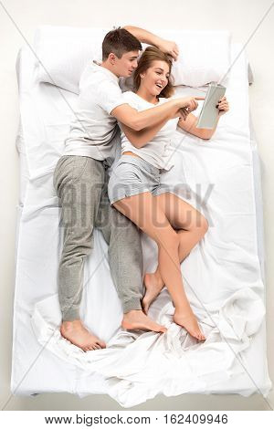 The young lovely couple lying in a white bed with laptop, love lconcept, top view