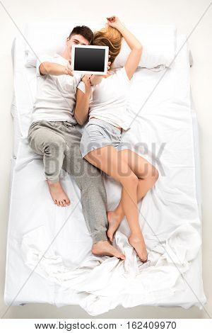 The young lovely couple lying in a white bed with laptop, love lconcept, top view