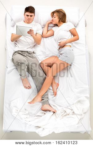 The young lovely couple lying in a white bed with laptop, love lconcept, top view