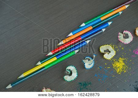 Color pencils with color pencils shave on black wooden background wiht text space