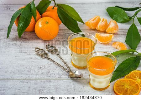 Delicious and rich in vitamins panna cotta with tangarine jam, tangarines and slice of tangarines on a white wooden table