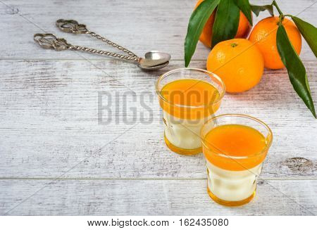 Delicious and rich in vitamins panna cotta with tangarine jam, tangarines and slice of tangarines on a white wooden table