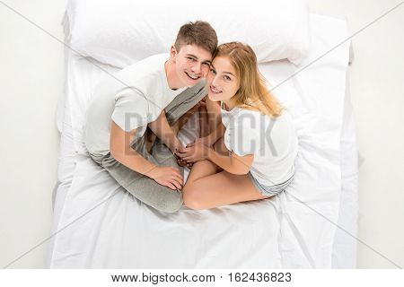 The young lovely couple sitting in a white bed, love lconcept, top view