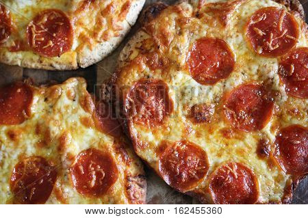 A group of small personal pan handmade fresh pepperoni pizzas are sitting on a wooden table.