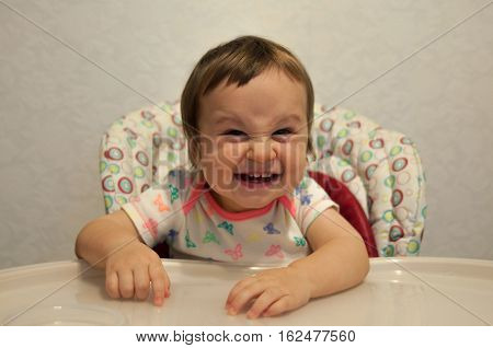 Concept of baby feeding hungry child good appetite food. Portrait of happy smiling cunning baby girl in high chair