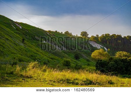 Green chalk hills under a cloudy sky. The multilayered archaeological monument - Krapivinskaya settlement Belgorod region Russia.