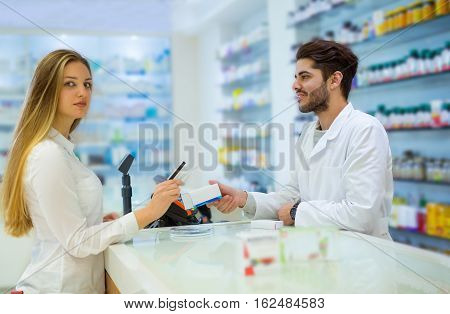 Experienced pharmacist counseling female customer in modern pharmacy and woman pays with credit card