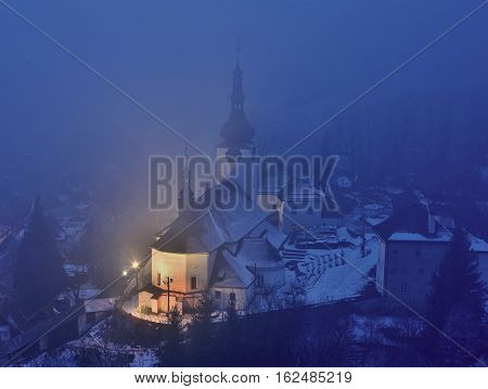 Winter in Slovakia. Old mining village. Historic church in Spania dolina. Fog at night.