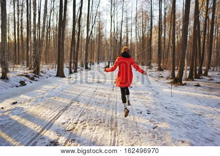 Young slender girl in a red coat runs along a snowy path in the Park fun bouncing and waving his arms.