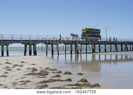 Victor Harbor SA Australia - Dec 20 2016: Horse Drawn Tram filled with tourists traveling along the bridge from Granite Island all reflected in the shallow water leeding up to the shore.