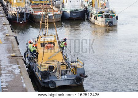 MOSCOW, RUSSIA - NOVEMBER 11, 2016: State Unitary Enterprise Mosvodostok performs recovery vessels on coastal winter parking. Several workers slingers hooked to the vehicle chain slings.