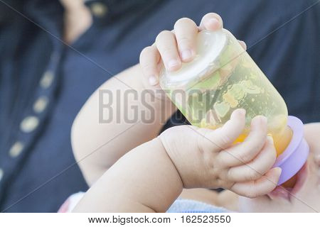 hand of baby holding orange juice bottle suck in embrace mother
