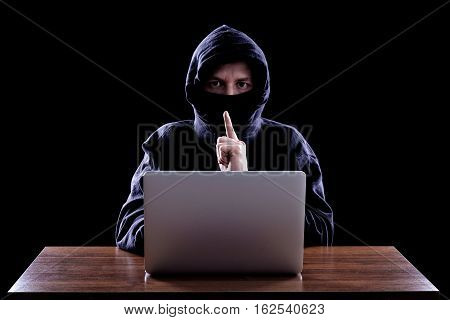 Hooded computer hacker stealing information with laptop. Dark background