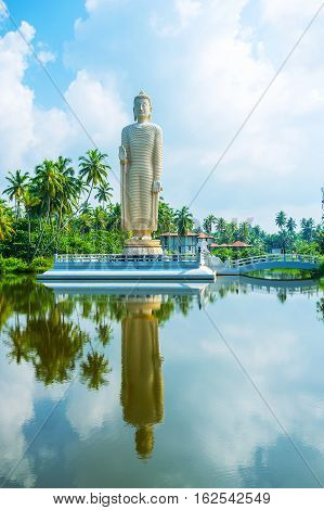 The Tsunami Memorial Buddha Statue reflects in waters of the calm river Peraliya Sri Lanka.