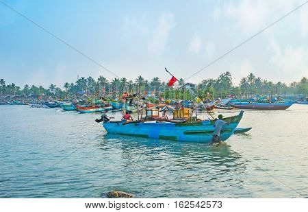 HIKKADUWA SRI LANKA - DECEMBER 5 2016: The fishermen back to the harbor and steer the colorful wooden catamaran boat to shore on December 5 in Hikkaduwa.