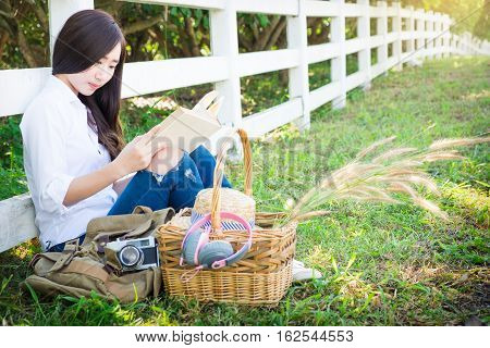 Pretty relaxed young asian woman reading a book at the lawn garen with sun shining vintage tone.