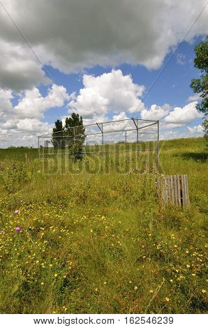 A former rural baseball is forgotten, neglected with only the backstop and garbage receptacle as former evidence of the athletic field.