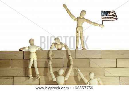 Model of anonymous people climbing a wall. One of the people holds the USA flag. Connotations are of illegal immigration at a border wall but also aspects of teamwork and success.