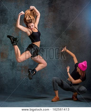 The two attractive girls dancing twerk iat the blue studio background
