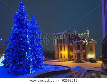 Illuminated House with Chimaeras or Horodecki House (Kiev). Night scene. Illuminated fir-trees in foreground. Building and street are powdered with snow.