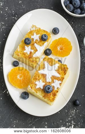 Two servings of homemade juicy mandarin biscuit with asterisks from icing sugar on a dark background. Top