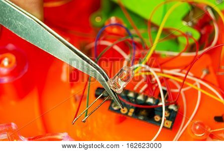hands holding tweezers adjusting a hand made electronic part
