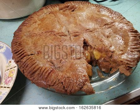 Large homemade apple pie with one piece cut out.