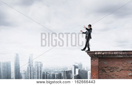 Businessman with blindfolder on eyes walking on building top