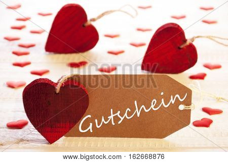 Label With German Text Gutschein Means Voucher. Many Red Heart. Wooden Rustic Or Vintage Background.