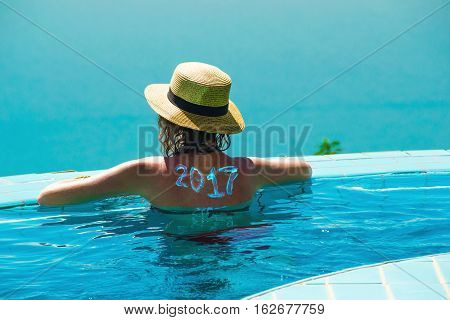 Photo of the Woman from behind in hat and infinity pool looking away. New travel season concept. 2017 written on back by suncream