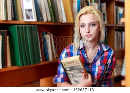 Young girl on the background of shelves with books holds in his hands the book