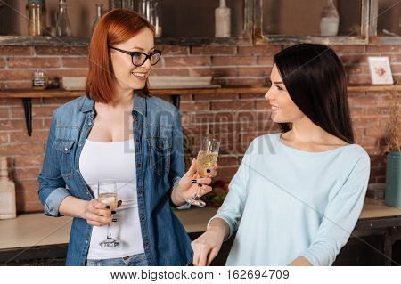 Take it. Red haired woman wearing eyeglasses holding two bocals of fizzy drink while offering one glass to her friend