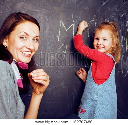 cute cheerful teacher with little pupil in classroom at blackboard learning, happy smiling, lfestyle people concept close up