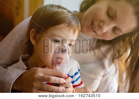 Young woman with son doing inhalation with a nebulizer at home. Mother of a young child making inhalation