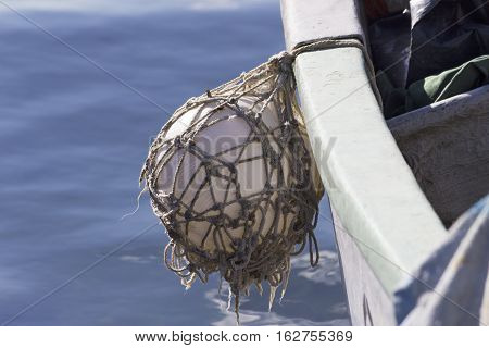 fender ball hanging off side of the hull of a fisher boat with blue sea