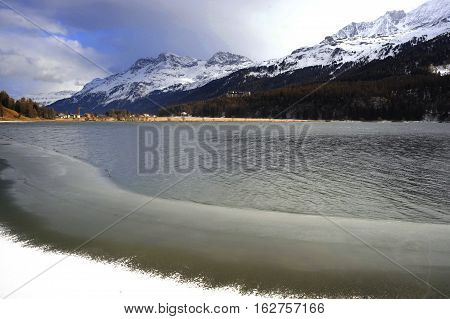 amazing beautiful scenic view of winter snow mountains landscape and frozen lake in the swiss Alps in Engadin Sils Maria and Saint Moritz village in Switzerland on a cold sunny day